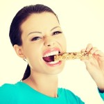 32929997 - young woman eating cereal candy bar, isolated on white